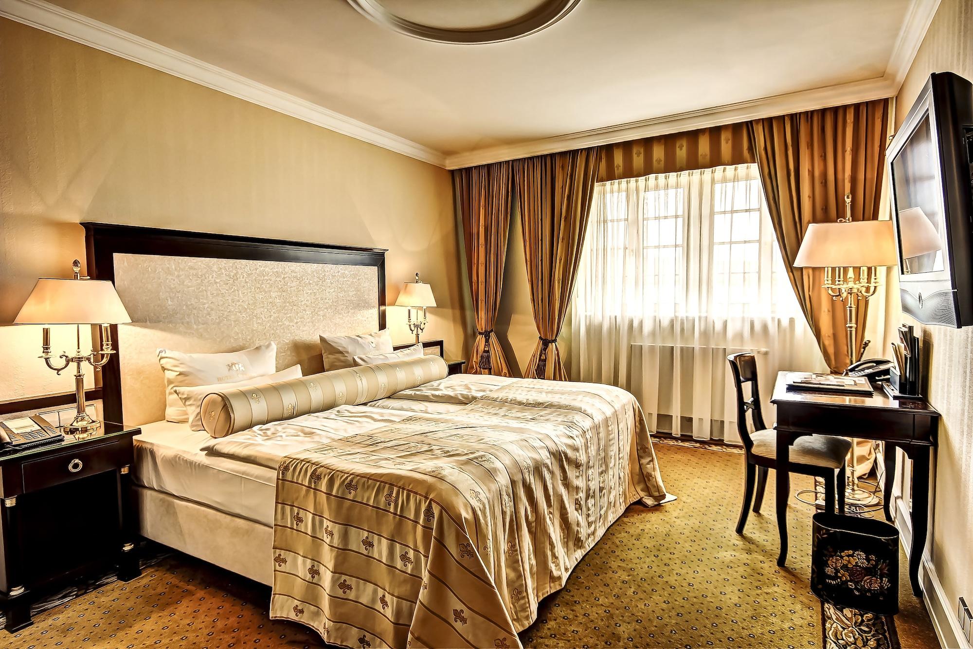 Hotel Suitess Δρέσδη Εξωτερικό φωτογραφία The photo shows a luxurious hotel room. It features two neatly made beds with decorative bed linens and a large upholstered headboard. There are elegant curtains covering the window, allowing natural light to enter the room. 

In front of the window,