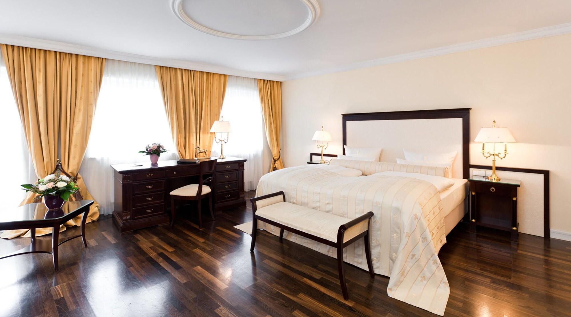 Hotel Suitess Δρέσδη Εξωτερικό φωτογραφία The photo shows an elegantly designed bedroom. It features a large bed with a light-colored bedspread, accompanied by a decorative bench at the foot of the bed. The room is adorned with warm yellow curtains that frame two windows, allowing natural li