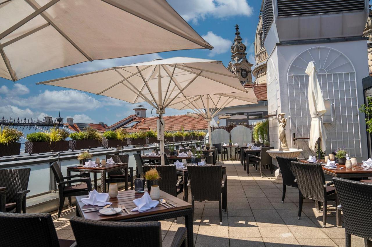 Hotel Suitess Δρέσδη Εξωτερικό φωτογραφία The photo shows an outdoor dining area, likely on a rooftop terrace. There are several tables set with utensils and napkins, all arranged neatly. Large umbrellas provide shade for the diners. The surrounding area includes potted plants, and in the ba