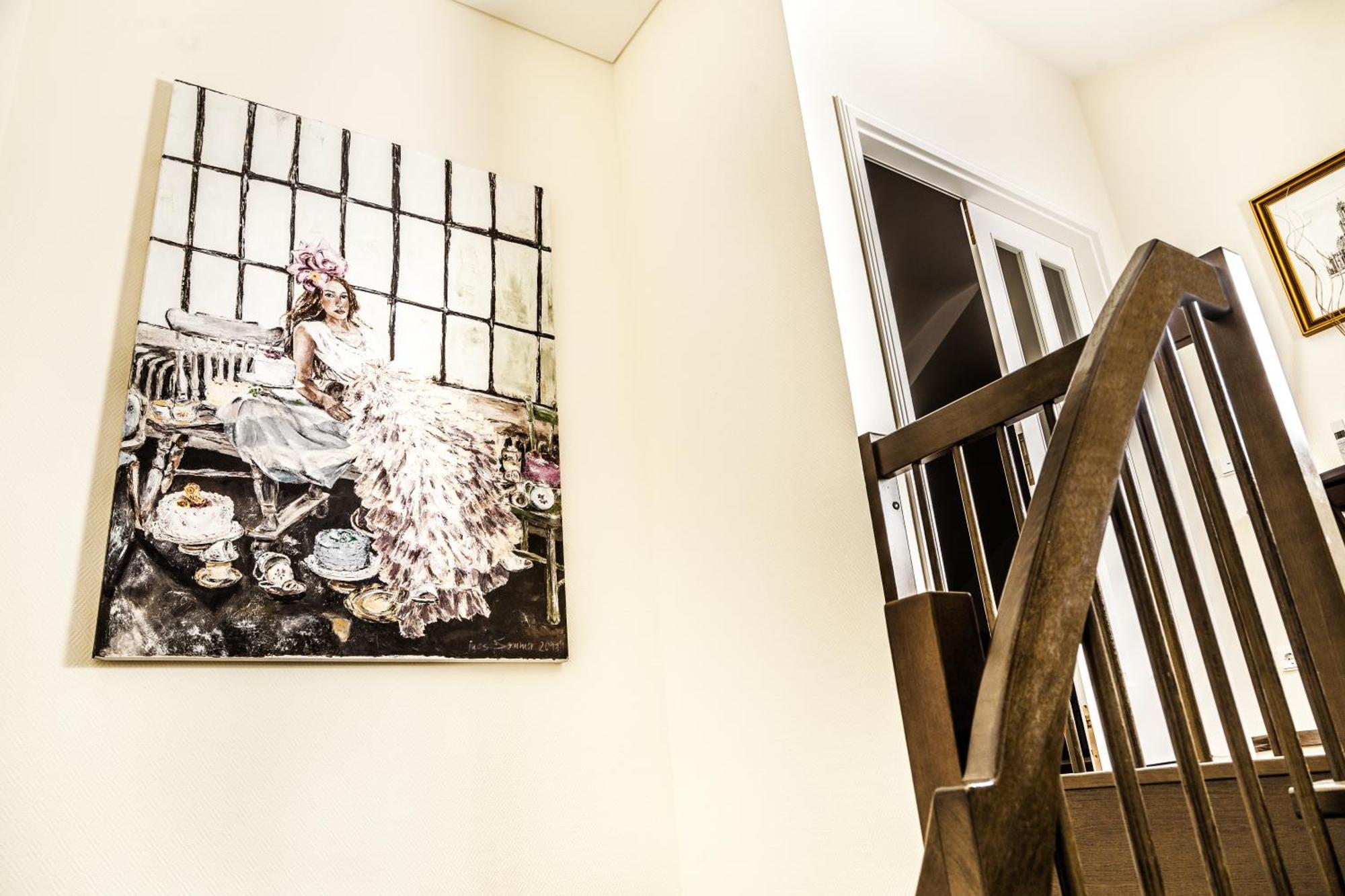 Hotel Suitess Δρέσδη Εξωτερικό φωτογραφία The photo shows a staircase with a wooden railing leading up, and on the wall beside it hangs a large artwork. The artwork features a figure, likely a woman, dressed in a gown, sitting amidst a decorative setup that includes teacups and other items. 