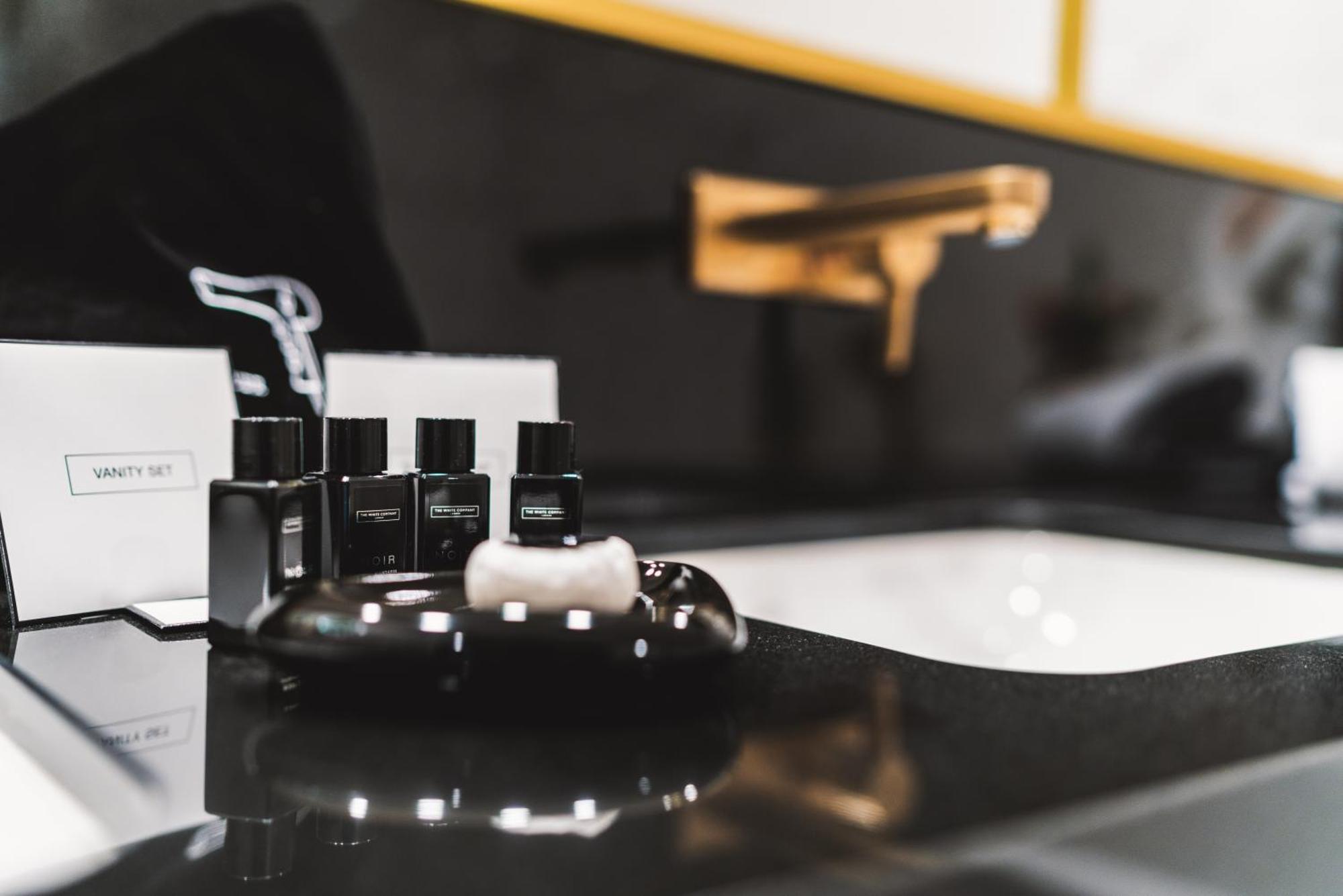 Hotel Suitess Δρέσδη Εξωτερικό φωτογραφία The photo shows a modern bathroom countertop featuring a sleek black surface. On the countertop, there are several small black bottles, likely containing toiletries or grooming products. These bottles are arranged neatly on a black dish, which also h