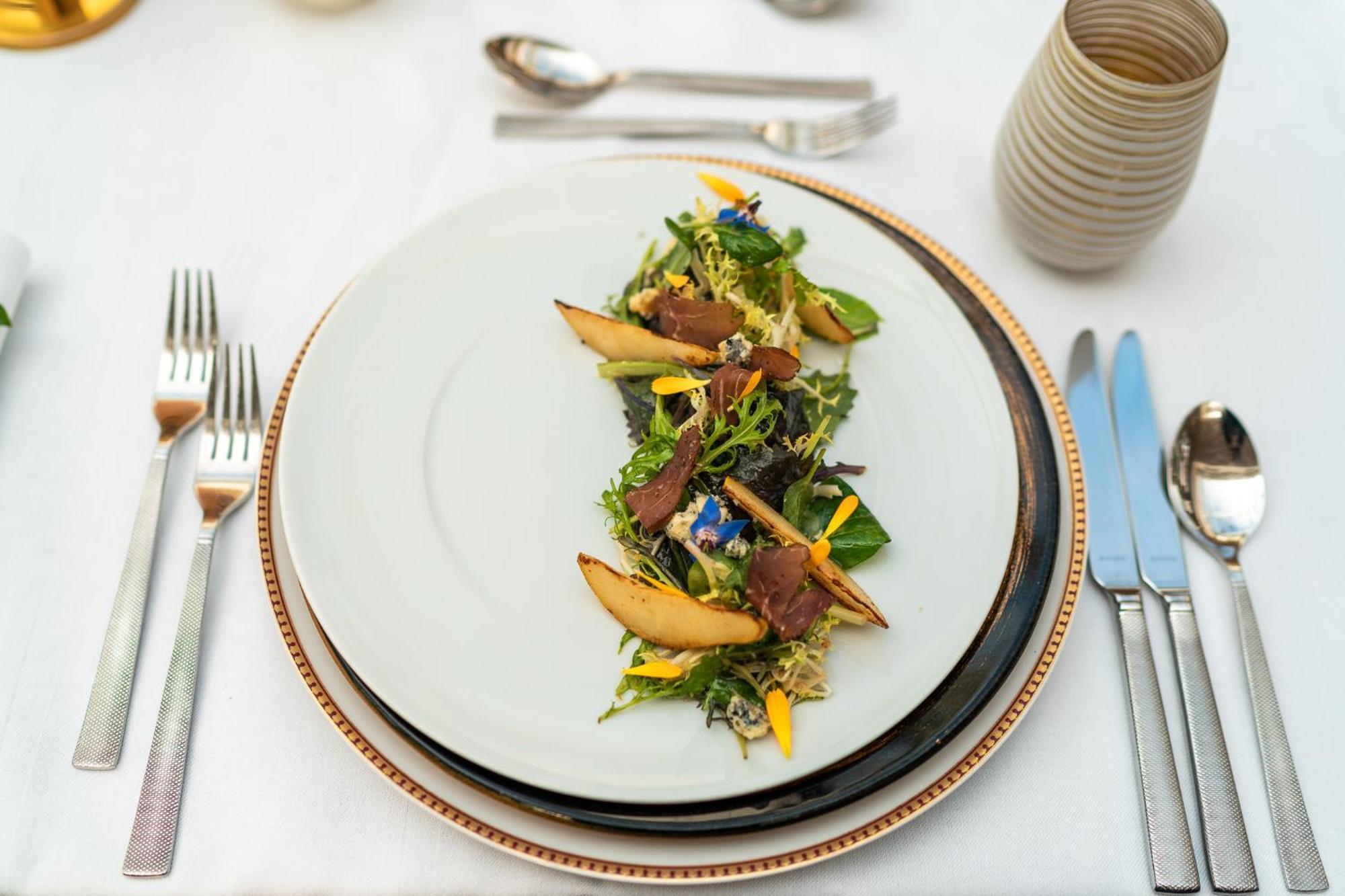 Hotel Suitess Δρέσδη Εξωτερικό φωτογραφία The photo shows a beautifully plated salad arranged on a white dish. The salad features a mix of greens, possibly including lettuce and other fresh leaves, and is garnished with slices of what appear to be roasted or grilled pears. There are colorful