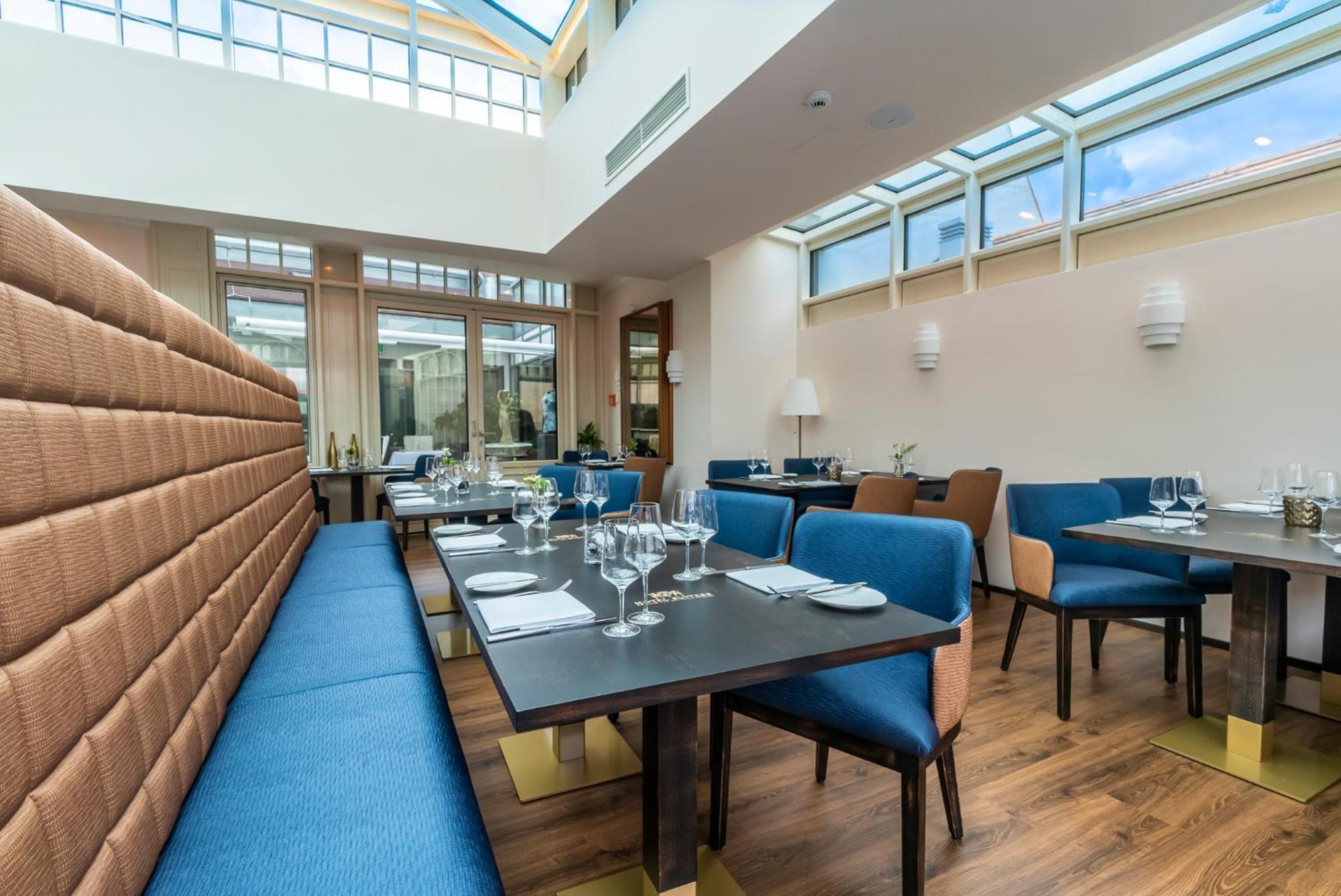 Hotel Suitess Δρέσδη Εξωτερικό φωτογραφία The image shows a modern restaurant interior. It features tables set for dining, with blue and brown upholstered chairs. The tables have glassware and table settings, indicating readiness for guests. The space is bright, with large windows allowing n