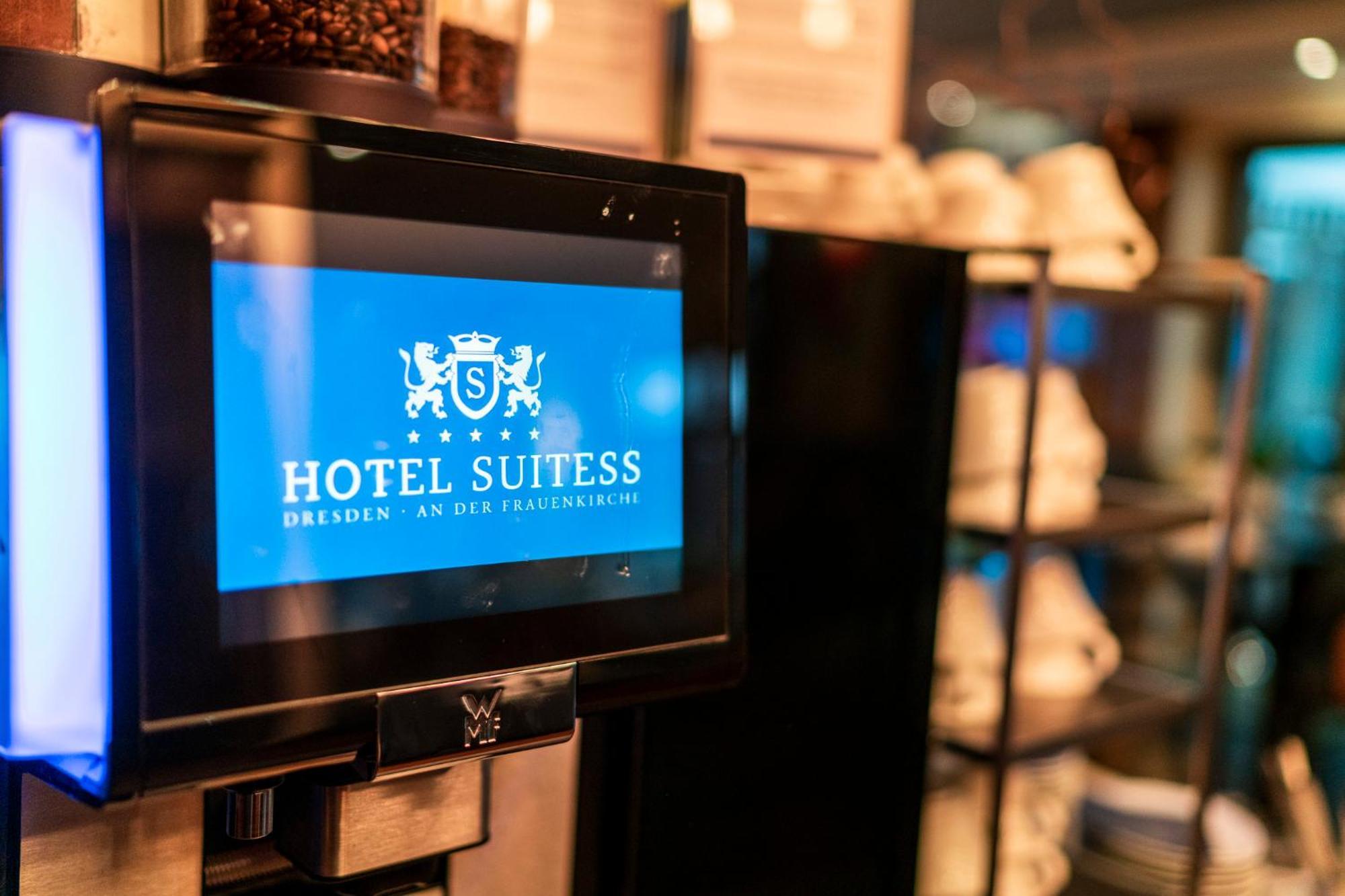 Hotel Suitess Δρέσδη Εξωτερικό φωτογραφία The image shows a digital display featuring the logo of "Hotel Suitess" located in Dresden, along with the phrase "an der Frauenkirche." The screen is prominently displayed in a hotel setting, suggesting it is likely used for informational purposes o