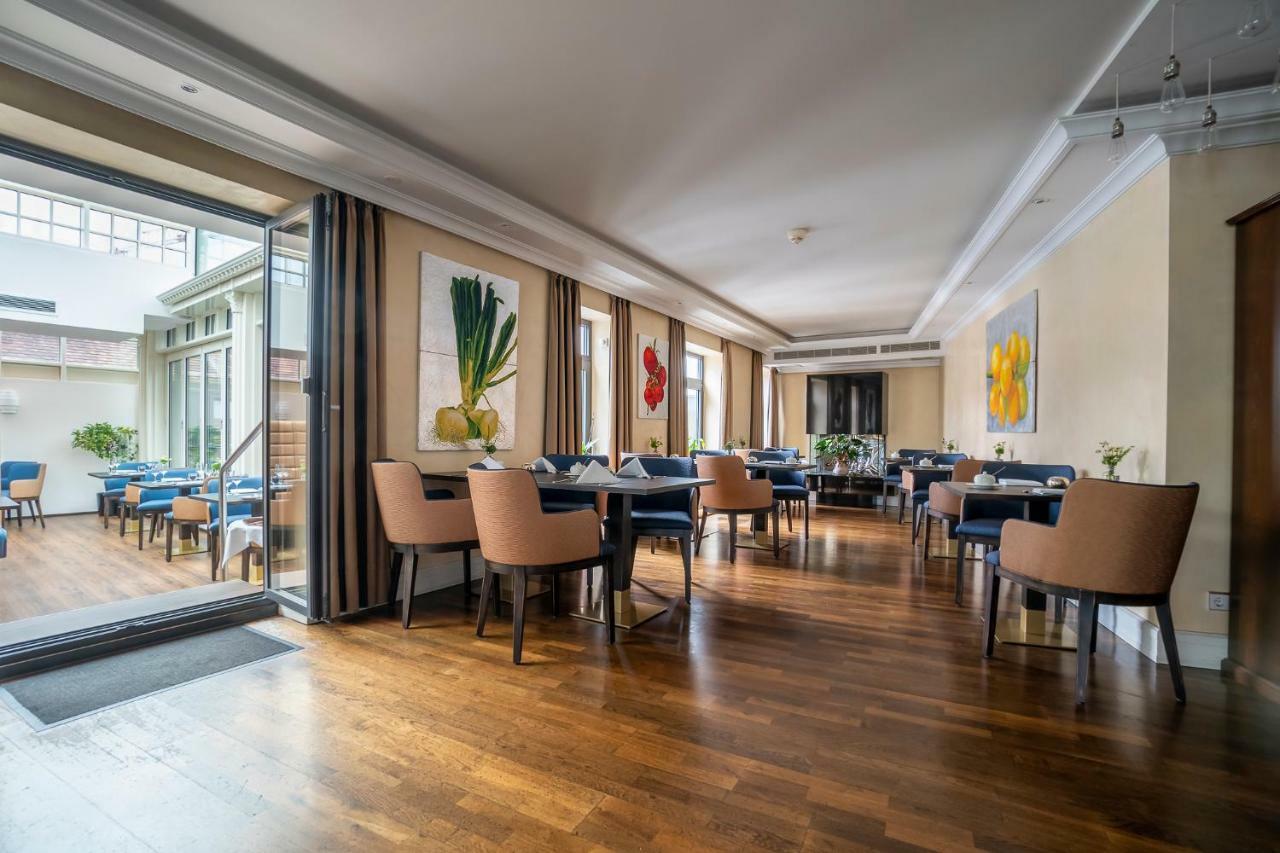 Hotel Suitess Δρέσδη Εξωτερικό φωτογραφία The photo displays a modern dining area with a warm and inviting atmosphere. The room features hardwood flooring and large windows that allow natural light to fill the space. There are several tables set up with blue tablecloths and comfortable chair